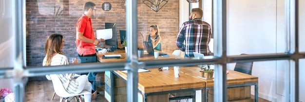 A shared co-working space within a co-living building featuring several individuals working at desks with laptops. The space is brightly lit with large windows and features ergonomic chairs and a modern, minimalist design.