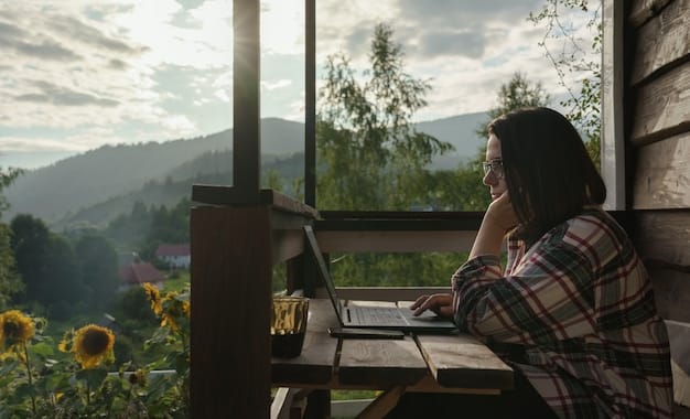 A person smiling and working on a laptop inside a tiny house, with a beautiful landscape visible through the window.