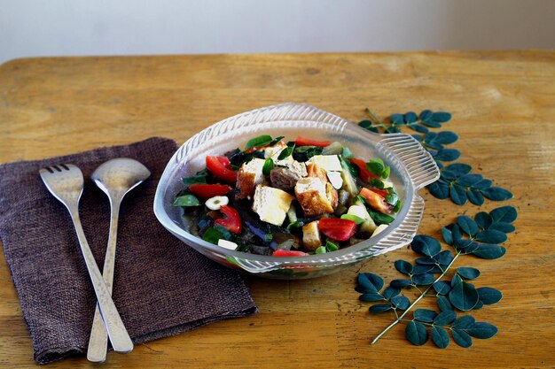 A colorful and healthy salad with mixed greens, grilled chicken, avocado, tomatoes, and a light vinaigrette dressing, presented in a clear bowl on a wooden table.